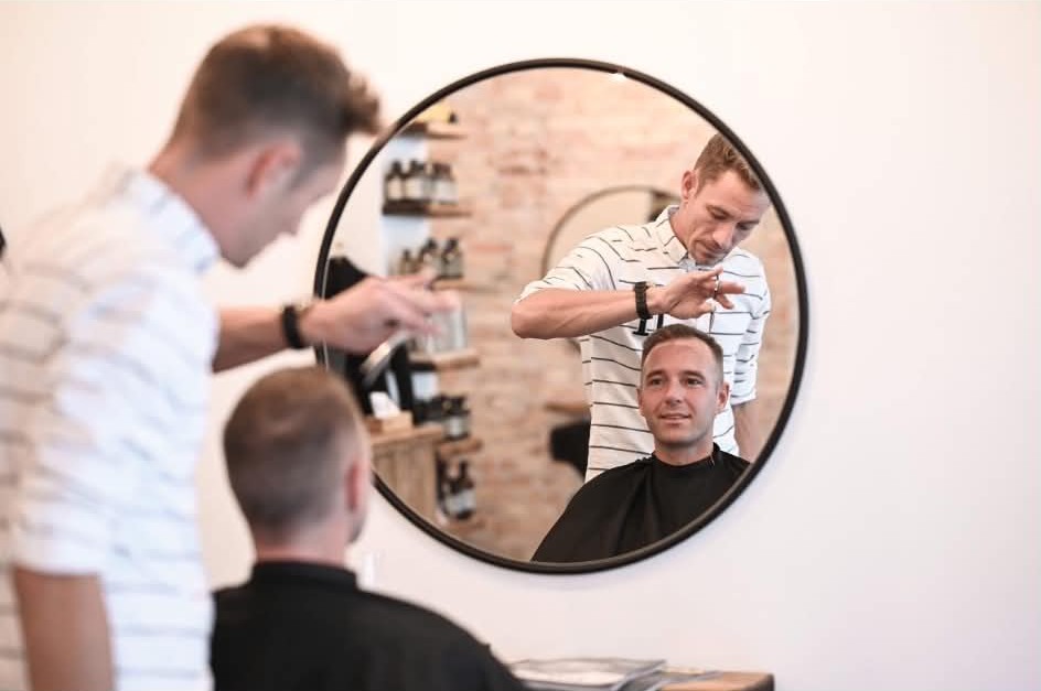 Mikkel Emil klipper en kunde foran spejlet hos CutsByME